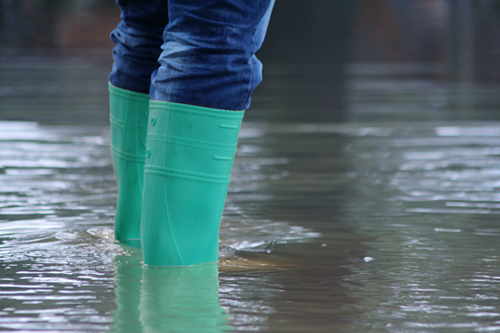 A person wading through flood waters in rubber boots.